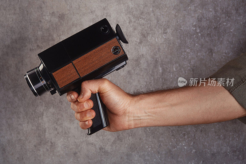 摄像机操作员拿着老式模拟Super8, 8毫米电影摄像机在混凝土墙前。把相机对准枪